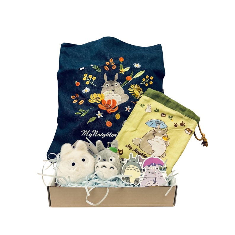 May include: A gift set featuring items from the animated film, "My Neighbor Totoro." Includes a denim tote bag with floral and Totoro embroidery, a drawstring bag, plush toys, and character stickers, all presented in a cardboard box.