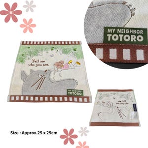 May include: A beige My Neighbor Totoro themed towel, approximately 9.8 x 9.8 inches, featuring an illustration of Totoro and a girl. The towel has a brown border and the text "Tell me who you are."