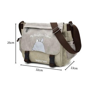 May include: Canvas messenger bag in beige and brown, featuring a flap with the text "My Neighbor Totoro" and an illustration of Totoro. The bag measures 32cm wide, 25cm high, and 13cm deep.