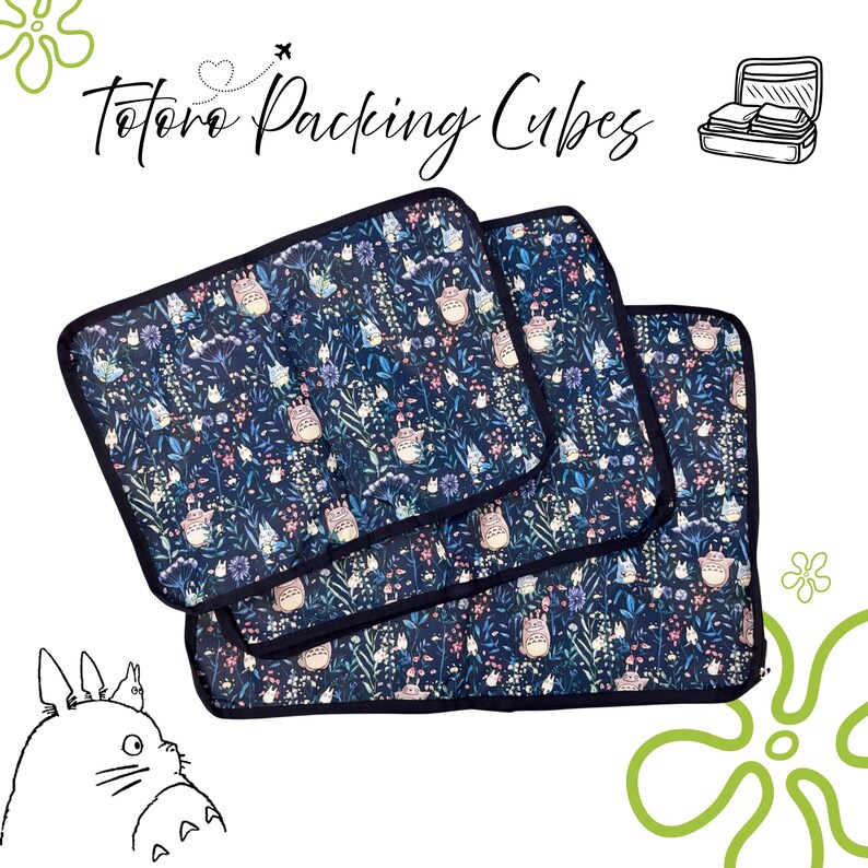 Puede incluir: Tres cubos de embalaje azul marino con un estampado floral y del personaje Totoro. Los cubos tienen un borde negro y est&aacute;n apilados. El texto "Totoro Packing Cubes" est&aacute; escrito en cursiva en la parte superior de la imagen.