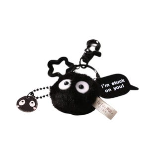 May include: Black plush keychain with a round, fuzzy black character with white eyes. The keychain has a metal ring and a black tag that says "I'm stuck on you!"