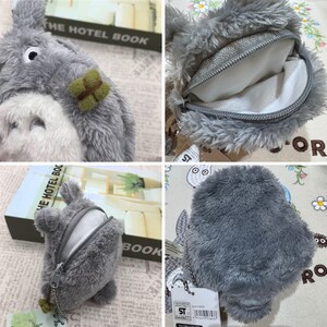 May include: A gray plush Totoro coin purse with a zipper opening. The purse has a small green leaf detail on the side. The purse is shown in different angles, including the inside of the purse.