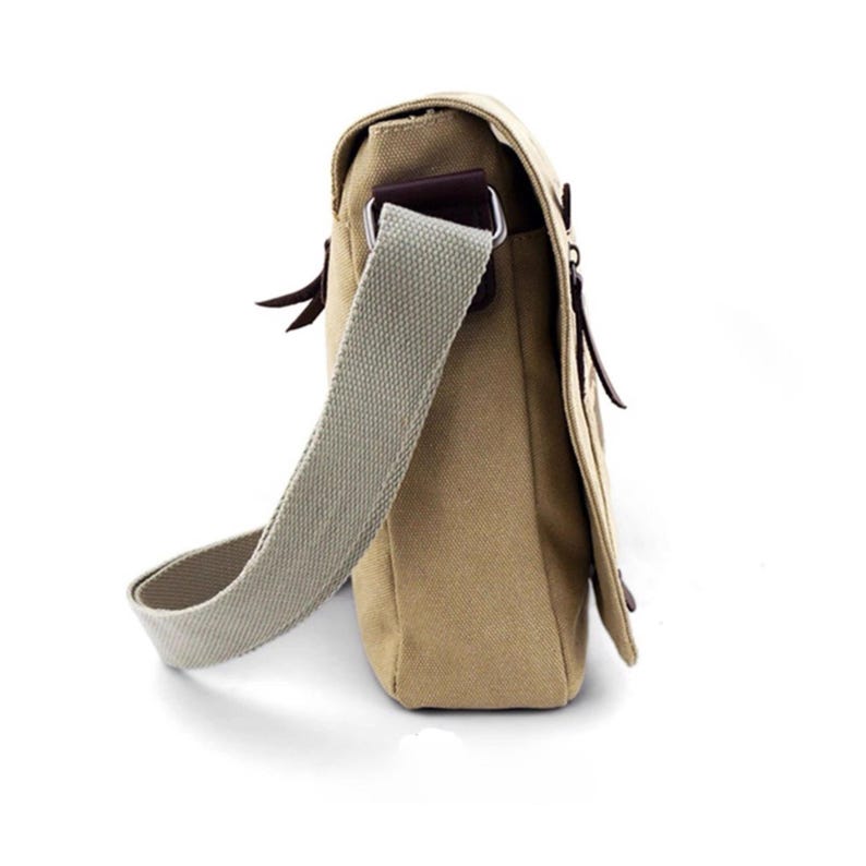 May include: A tan canvas messenger bag with a light gray adjustable shoulder strap. The bag features a flap closure with brown leather accents and a metal buckle. The bag is designed for carrying items and has a casual style.