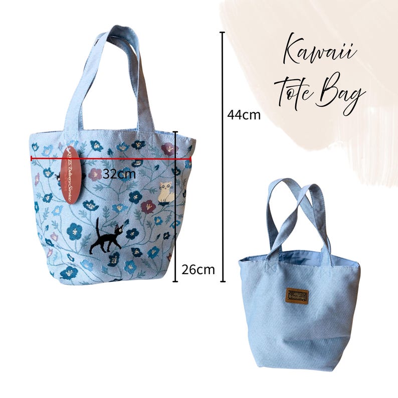 Pu&ograve; includere: Una borsa tote azzurra con un design floreale e di gatto. La borsa &egrave; alta 44 cm, larga 32 cm e profonda 26 cm. Le parole "Kawaii Tote Bag" sono scritte in corsivo. La borsa ha due manici e una piccola etichetta.