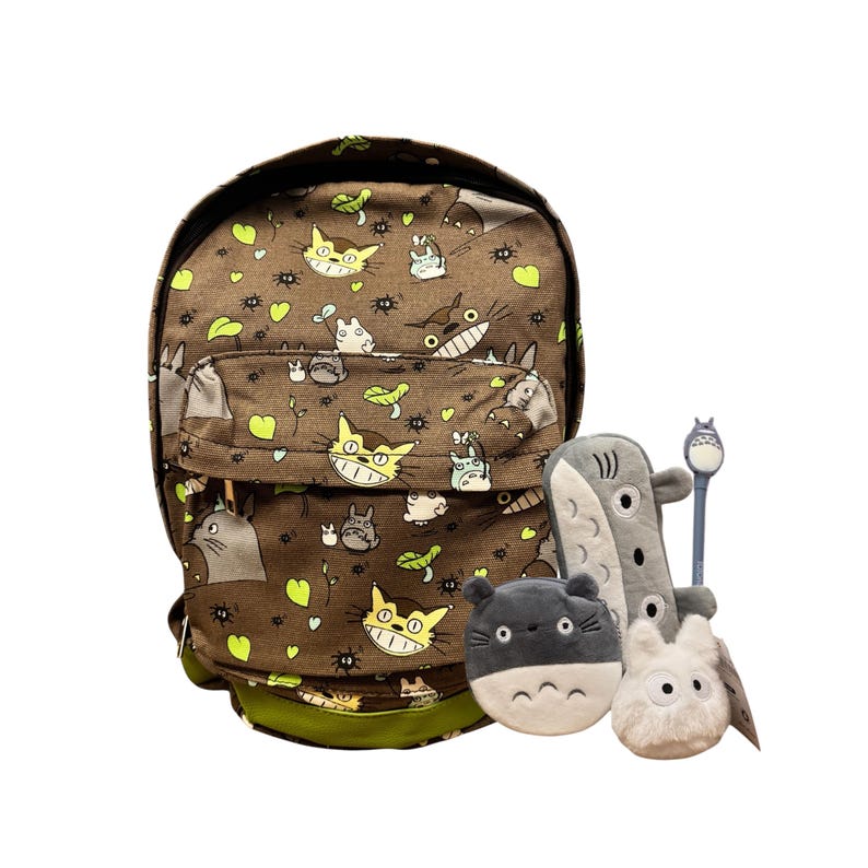 May include: Brown backpack patterned with cartoon characters, green leaves, and yellow hearts. Includes a grey plush shark, a grey plush Totoro, a white plush Totoro, and a blue and grey Totoro spoon.