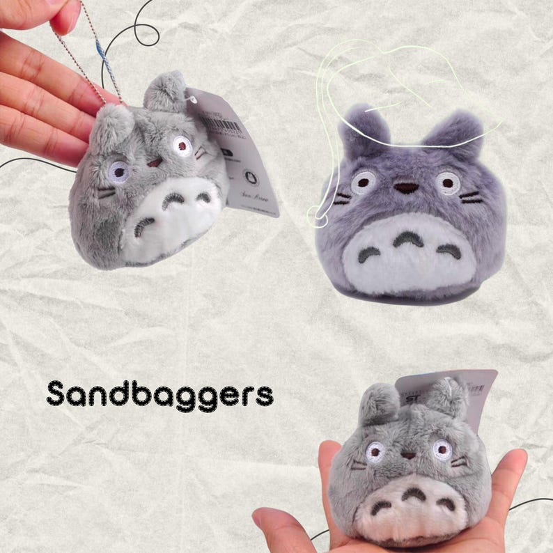May include: Three plush gray character keychains with white bellies, black whiskers, and red eyes. The keychains are in the shape of a cartoon character. The word "Sandbaggers" is written in black text at the bottom of the image.