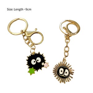 May include: Two gold keyrings with black and white enamel charms. One charm is a black and white cartoon character with large eyes and a spiky body. The other charm is a black and white cartoon character with large eyes and a spiky body with a gold outline. Size: Length ~9cm.