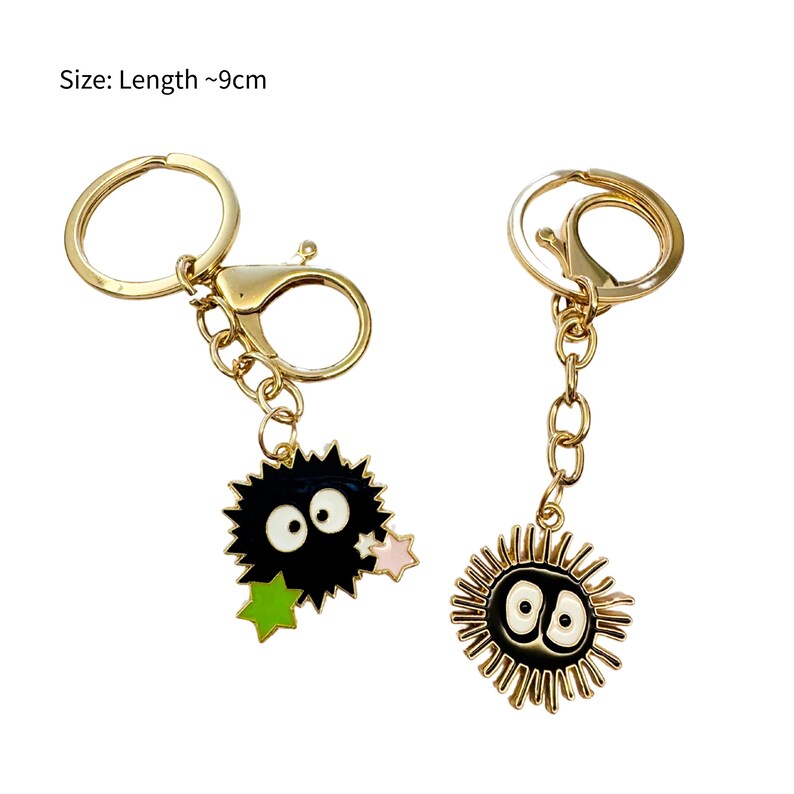 May include: Two gold keyrings with black and white enamel charms. One charm is a black and white cartoon character with large eyes and a spiky body. The other charm is a black and white cartoon character with large eyes and a spiky body with a gold outline. Size: Length ~9cm.