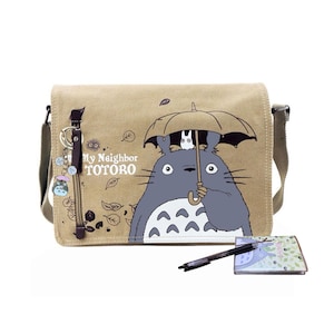 May include: Beige canvas messenger bag featuring a Totoro illustration with an umbrella. The bag has a flap closure, a shoulder strap, and a keychain with a Totoro charm. The text "My Neighbor TOTORO" is printed on the bag.
