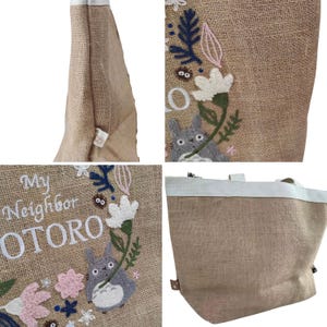 Puede incluir: Un bolso tote de yute beige con ribetes y asas blancas. El bolso presenta un dise&ntilde;o bordado de un personaje de dibujos animados gris, flores y el texto "My Neighbor TOTORO". El bolso tote es de color marr&oacute;n claro.