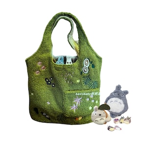 K&ouml;nnte beinhalten: Eine gr&uuml;ne Tragetasche mit gestickten Blumen- und Blattmotiven und einer Tasche. Die Tasche hat zwei kleine Zeichentrickfiguren in der Tasche. Ebenfalls enthalten sind drei Pl&uuml;schfiguren von Totoro und drei Totoro-Anstecknadeln.