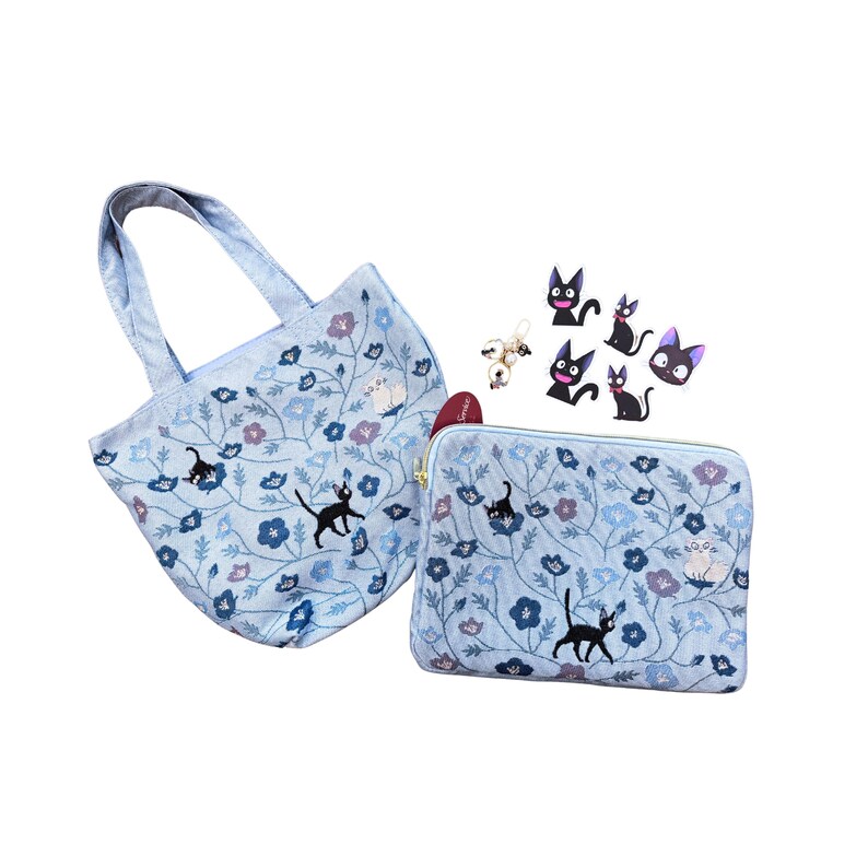 May include: A light blue tote bag and zippered pouch set with a floral and cat design. The set includes a tote bag with handles and a matching zippered pouch. Several black cat pins and a small white cat pin are also included.