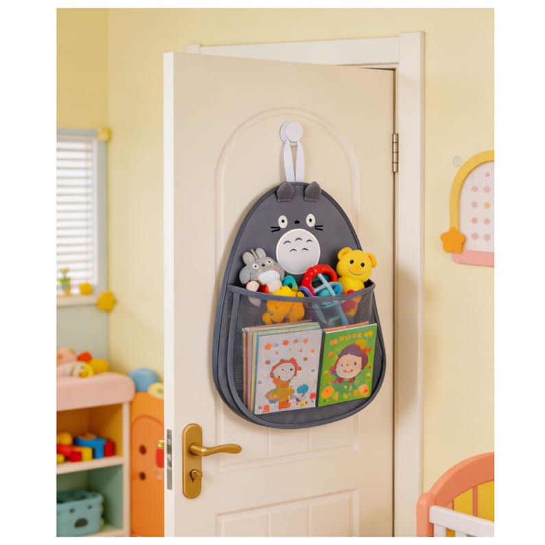 Puede incluir: Un organizador de puerta de tela gris con forma de personaje de dibujos animados, con dos bolsillos de malla llenos de juguetes y libros. El organizador cuelga de un gancho blanco en una puerta blanca en una habitaci&oacute;n infantil.