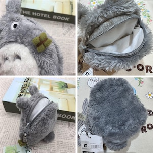 May include: A grey Totoro-shaped coin purse with a zip closure. The purse has a fluffy texture and a small green and brown accent. The interior is white, and a silver chain is attached. A tag with text is visible.