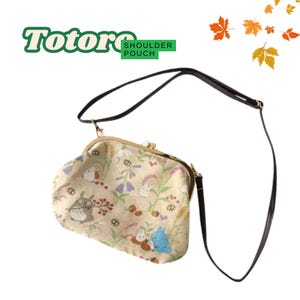 May include: A beige shoulder pouch with a floral and Totoro character print. The bag has a gold-colored clasp and a black strap. The text "Totoro Shoulder Pouch" is in the upper left corner.