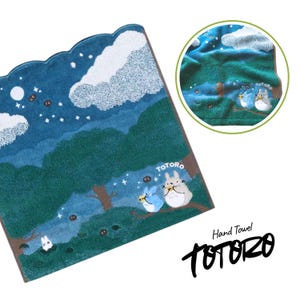 Puede incluir: Una toalla de mano con una escena nocturna de bosque, nubes y estrellas. La toalla presenta una ilustraci&oacute;n de los personajes de Totoro. El texto "TOTORO" est&aacute; impreso en la toalla, junto con las palabras "Hand Towel".