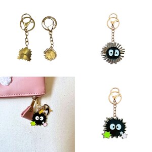 May include: Three gold keychains with different charms. One keychain has a gold star charm, another has a gold sun charm, and the third has a black and white cartoon character charm with a spiky body and large eyes.