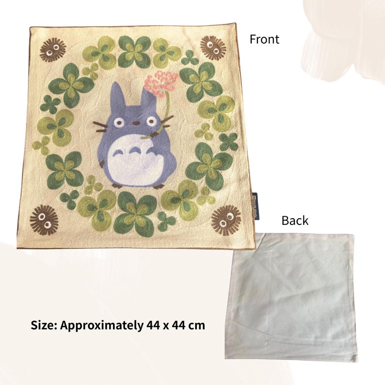 Puede incluir: Coj&iacute;n cuadrado beige con un personaje de dibujos animados, rodeado de tr&eacute;boles verdes. El personaje es azul con vientre blanco y sostiene una flor rosa. El coj&iacute;n mide aproximadamente 44 x 44 cm.