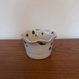 May include: A small, white ceramic planter with a scalloped rim and green speckles.