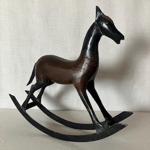May include: A decorative rocking horse sculpture featuring a dark brown wooden body with a smooth finish. The head, neck, and legs are painted in a solid black color. The horse is mounted on two curved black metal rockers that allow for movement.
