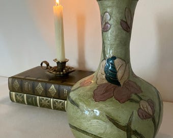 May include: A light green vase with a textured surface featuring painted floral motifs in shades of pink, brown, and dark teal. The vase has a bulbous body, a slender neck, and a metallic rim at the top opening, showcasing a detailed botanical design.