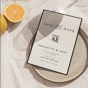 Puede incluir: Una tarjeta beige de guardar la fecha con texto negro y una simple ilustración de dos copas de champán. El texto dice "Save the Date", "Bridgette & Cody", "invite you to celebrate their wedding", "12 31 29", "New York, New York", y "formal invitation to follow".