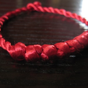 May include: A red braided cord bracelet with a knotted design.