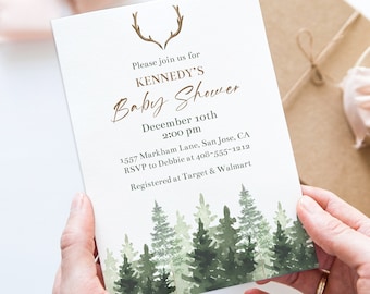 May include: A baby shower invitation with a forest design. The invitation reads "Please join us for KENNEDY'S Baby Shower December 10th 2:00 pm". The invitation is held by hands, with a gift box and ribbon in the background.