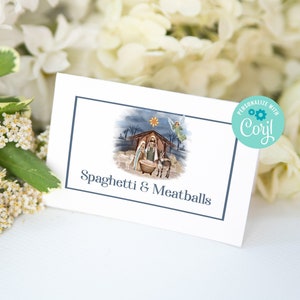 May include: A white card with a blue border features an illustration of the Nativity scene and the text "Spaghetti & Meatballs." The card is surrounded by white flowers and greenery, with a teal circle that says "Personalize with Corjl!"