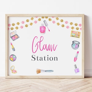 May include: A white sign with a gold frame and the text "Glam Station" in pink lettering. The sign is decorated with watercolor illustrations of makeup products, including lipstick, eyeshadow, nail polish, and brushes.