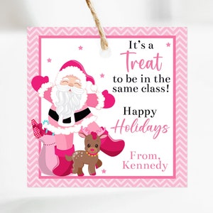 Puede incluir: Una etiqueta de regalo navideña rosa y blanca con una ilustración de Papá Noel. La etiqueta presenta el texto "It's a Treat to be in the same class! Happy Holidays From, Kennedy" en rosa. También se muestra un reno y una bolsa de regalo.