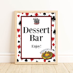 May include: A white sign with a red and black playing card border. The sign says "Dessert Bar Enjoy!" with a stack of poker chips and a roulette wheel with playing cards on top.