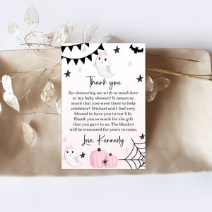 May include: A baby shower thank you card with a ghost, pumpkins, and spiderweb design. The card includes the text "Thank you" and a personalized message. The card is on a beige tray with decorative sprigs.