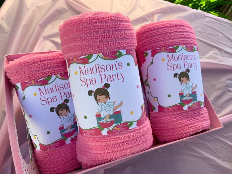 K&ouml;nnte beinhalten: Drei rosa Handt&uuml;cher in einer Geschenkbox mit personalisierten Etiketten, auf denen "Madison's Spa Party" steht. Jedes Etikett zeigt ein Cartoon-M&auml;dchen in einem Bademantel und einem Blumendesign.