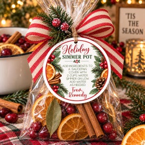 May include: A clear plastic bag filled with dried orange slices, cinnamon sticks, cranberries, and a bay leaf. A round tag reads Holiday Simmer Pot with instructions and the name Kennedy. The bag is tied with a red and white striped ribbon.