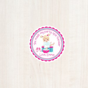 May include: Round pink and blue favor tag with a white background. The tag features a cartoon girl in a white robe with blonde hair, sitting in a foot bath. The text reads "You made my party spa-tacular. Love, Emma."