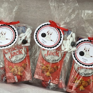 May include: Three clear plastic bags filled with party favors for a bowling themed party. Each bag contains a small box of Cracker Jack popcorn, a small black bowling ball, and several white plastic bowling pins. Each bag has a round tag attached with the text "It was a BALL having you at my party!" with a bowling ball and pins graphic and the text "From Lily".