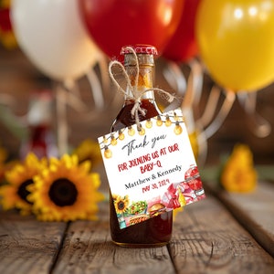 May include: A white thank you tag with red and black text that reads "Thank you for joining us at our Baby-Q Matthew & Kennedy May 30, 2024". The tag is tied to a small brown glass bottle with a brown cork.