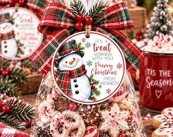 May include: A clear plastic bag filled with assorted holiday cookies and candies, tied with a red and green plaid ribbon and a round tag featuring a snowman illustration and the text: IT'S A treat WORKING WITH YOU! Merry Christmas FROM KENNEDY.