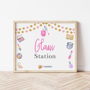 May include: A printable sign with the text "Glam Station" in pink lettering. The sign is decorated with watercolor illustrations of makeup products, including eyeshadow palettes, lipstick, nail polish, and brushes. A gold and pink garland is at the top of the sign.