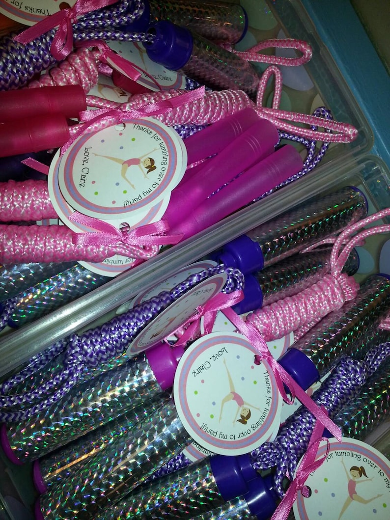 K&ouml;nnte beinhalten: Rosa und lila Springseile mit silbernem Glitzer-&Uuml;berzug und wei&szlig;en Etiketten mit der Aufschrift "Danke, dass du zu meiner Party gekommen bist! Liebe, Claire".