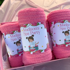 K&ouml;nnte beinhalten: Drei rosa Handt&uuml;cher mit floralen Etiketten, auf denen "Madison's Spa Party" steht und ein Cartoon-M&auml;dchen in einem Bademantel abgebildet ist.