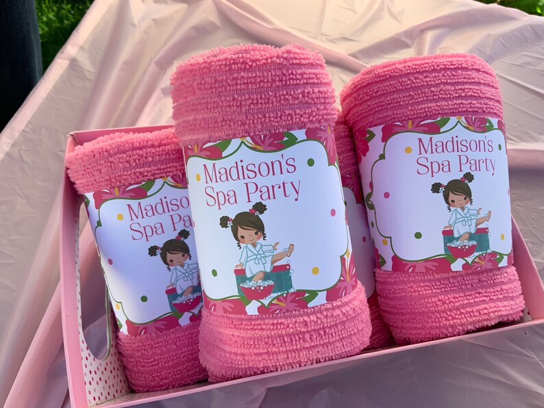 K&ouml;nnte beinhalten: Drei rosa Handt&uuml;cher mit floralen Etiketten, auf denen "Madison's Spa Party" steht und ein Cartoon-M&auml;dchen in einem Bademantel abgebildet ist.