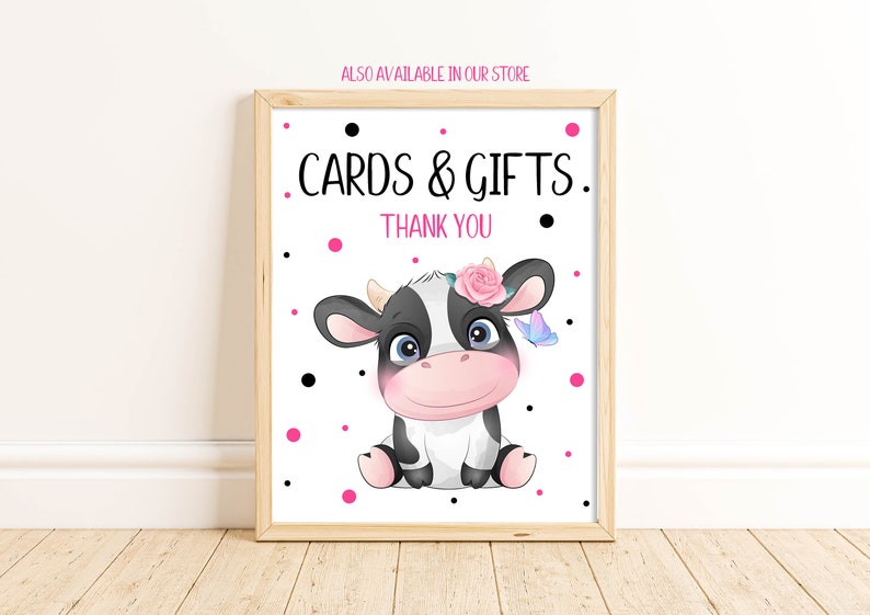 May include: A white sign with black polka dots and pink dots. The sign says "Cards & Gifts. Thank You" and features a cartoon black and white cow with a pink flower crown and a blue butterfly.