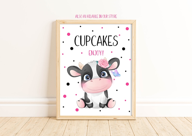 May include: A white sign with black polka dots and pink polka dots. The sign says "Cupcakes Enjoy!" and features a cartoon black and white cow with a pink flower and a blue butterfly.
