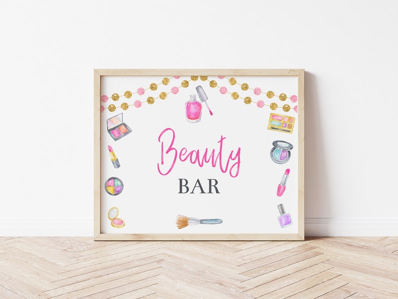 May include: A printable sign with the text "Beauty Bar" in pink script. The sign is decorated with watercolor illustrations of makeup products, including lipstick, eyeshadow, nail polish, and brushes. A gold and pink garland is at the top of the sign.
