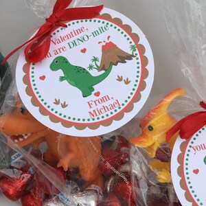 Puede incluir: Una bolsa de golosinas para el D&iacute;a de San Valent&iacute;n con una cinta roja, un juguete de dinosaurio y una etiqueta redonda que dice "Valentine, you are DINO-mite. From, Michael."