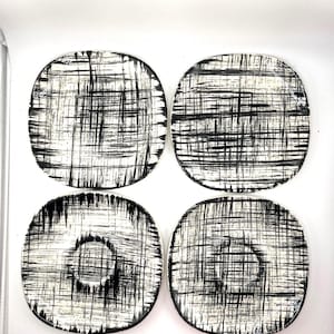 Puede incluir: Cuatro posavasos redondos con un diseño abstracto en blanco y negro. Los posavasos tienen un fondo blanco con un patrón de líneas negras. Dos posavasos tienen un círculo central sólido.
