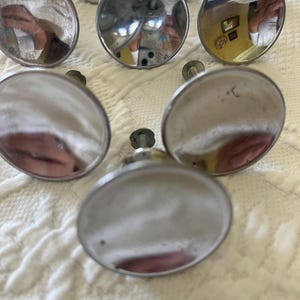 May include: A collection of seven circular cabinet knobs with a polished, reflective silver-tone finish. Each knob features a smooth, flat, round face that acts as a mirror, with a metal mounting screw extending from the center of the back side.