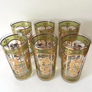 May include: Set of six vintage drinking glasses. Each glass features a clear body with a green band and gold filigree design around the rim. The glasses have a tall, slender shape, perfect for serving beverages.